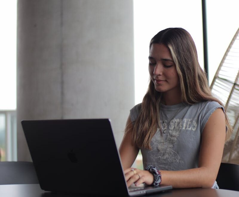 A young woman focused on her laptop, studying in a modern indoor setting.