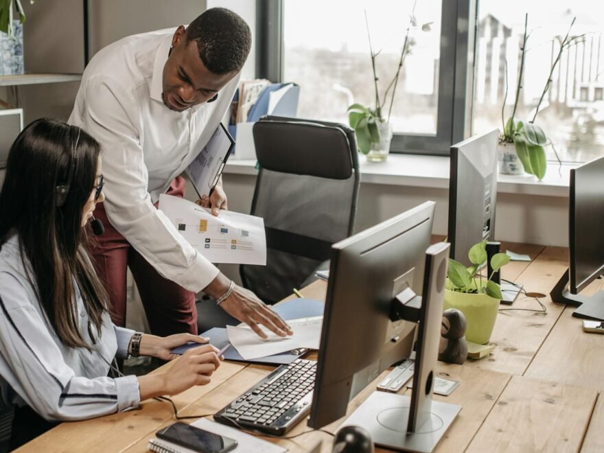 Two professionals discussing work at a computer in a bright, modern office space.